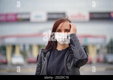 Giovane donna in maschera medica guarda via, in piedi sulla strada in città. Primo piano di donne che si proteggono dalle malattie a piedi. Concetto di minaccia di Foto Stock