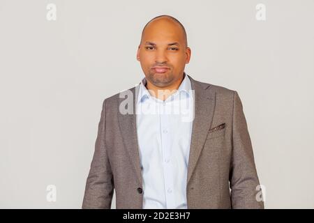 Primo piano di infelice uomo d'affari afro-americano in blazer arricciando le labbra e guardando la macchina fotografica, sconvolto su cattive notizie, in posa per una foto su sfondo grigio Foto Stock