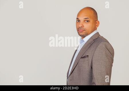 Bel giovane uomo d'affari afro-americano in giacca guardando la telecamera che tiene la testa in tre quarti con un'espressione seria sul viso. Posa per una foto su sfondo grigio. Foto Stock
