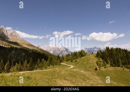 Strada per un piccolo rifugio appartato per pastori sulle Alpi italiane. Paesaggio delle Dolomiti, un prato verde e cielo nuvoloso sulla cima della montagna Foto Stock