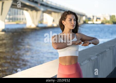 Adatta giovane donna atletica che allunga le braccia e il corpo sull'argine. Fitness femminile in leggings rosa facendo caldo allenamento all'aperto. Foto Stock