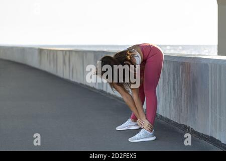 Donna atletica in gamba rosa in piedi su argine, stretching muscoli fare allenamento funzionale, fare esercizi per le gambe prima di un lavoro fuori. Gira Foto Stock