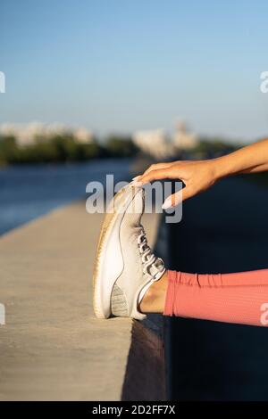 Primo piano di muscoli stretching femminile facendo allenamento funzionale, facendo esercizi per le gambe prima di un allenamento. Fitness, corsa urbana. Foto Stock