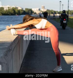 Donna atletica in gamba rosa in piedi su argine, stretching muscoli fare allenamento funzionale, fare esercizi per le gambe prima di un lavoro fuori. Gira Foto Stock