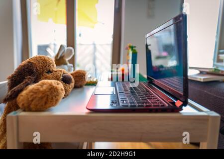 Divertente scenario di casa con un teddy farcito e il suo amico un coniglio che lavora a un computer portatile. Foto Stock