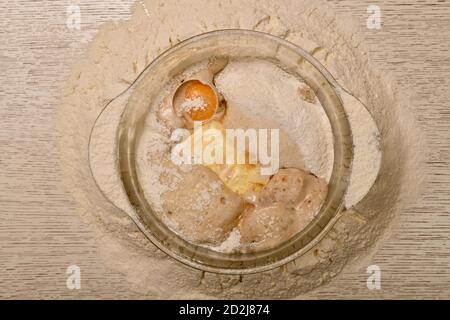 Una miscela di latte, uova, burro, zucchero, sale, lievito in polvere, vanillina e lievito al centro di un mucchio di farina di grano. Foto Stock