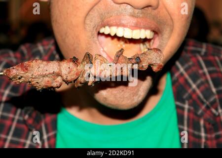 Un uomo che mangia Sate Klathak o Klatak Satay è un piatto di satay di capra o di mutton unico con bastone di acciaio, satay tradizionale da Yogyakarta, Indonesia. Foto Stock