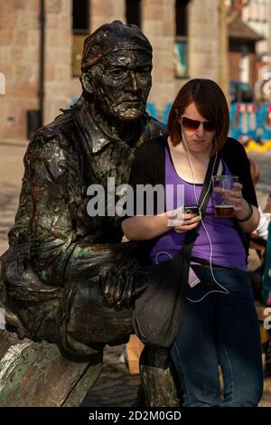 Bristol, UK 04/17/2010: Una giovane donna caucasica che ascolta musica, suona con il suo telefono e beve birra in tazza di plastica sta appoggiando sulla famosa J Foto Stock