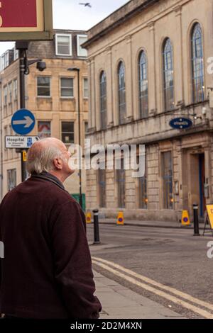 Bath, UK 03/06/2010: Un uomo caucasico anziano che indossa un cappotto invernale si trova sul marciapiede, guardando dall'altra parte della strada in un edificio storico in cit Foto Stock