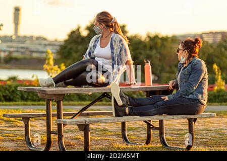 Arlington, VA, USA 10/02/2020: Due donne si rilassano al Gravelly Point Park al tramonto. Si siedono sul tavolo da picnic con la torre dell'aeroporto Reagan nel backg Foto Stock