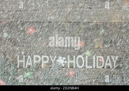 parole buone feste fatte da lettere di legno decorate con neve rami di albero di natale su sfondo grigio rustico di legno Foto Stock