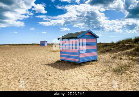 Great Yarmouth Beach Cabins in un giorno d'estate, tradizionale cabina inglese su una costa orientale, strisce orizzontali blu e rosa, cielo con nuvole Foto Stock