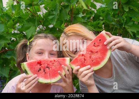 Due ragazze con fette di anguria vicino alle loro facce. Simbolo del sorriso. Il concetto di felice infanzia, tempo estivo, vacanze. Messa a fuoco selettiva, primo piano Foto Stock