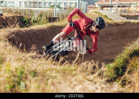 Sportswoman in caschetto nero e sportswear rosso con occhiali in mountain bike sulla pista di allenamento Foto Stock