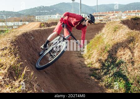 Sportswoman in caschetto nero e sportswear rosso con occhiali in mountain bike sulla pista di allenamento Foto Stock