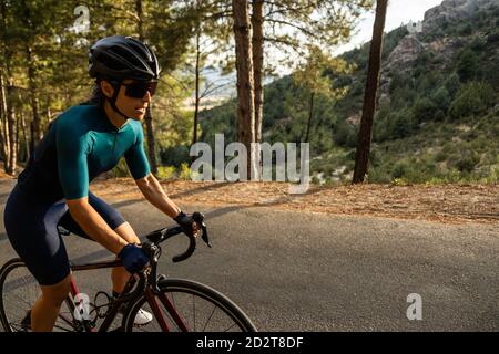 donna matura allenamento bici da strada, arrampicata su una strada di montagna, vista laterale Foto Stock