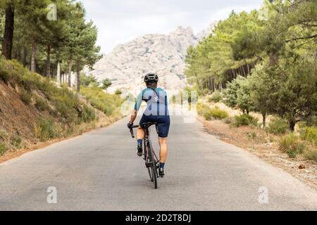 donna matura allenamento bici da strada, arrampicata su una strada di montagna, vista posteriore Foto Stock