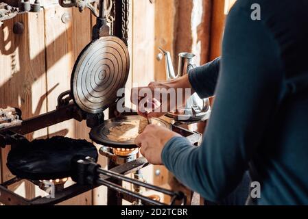 Un artigiano non riconoscibile tagliato utilizzando bastone mentre si arrotola caldo di fresco Waffle catalani al forno sulla cialda di ferro da stiro a gas fiamma Foto Stock