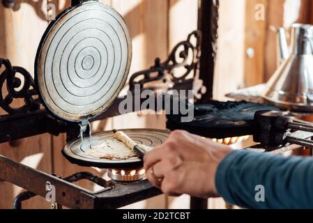 Un artigiano non riconoscibile tagliato utilizzando bastone mentre si arrotola caldo di fresco Waffle catalani al forno sulla cialda di ferro da stiro a gas fiamma Foto Stock