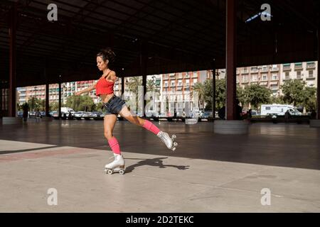 Equilibratura femminile concentrata sulla gamba mentre pattina a rulli su sport terreno in giornata di sole in città Foto Stock