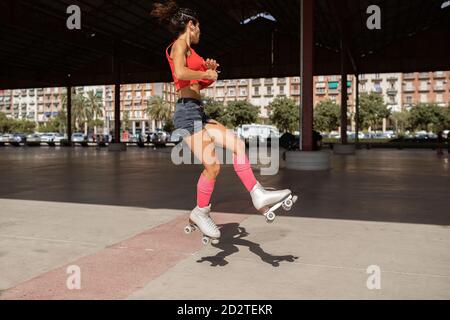 Equilibratura femminile concentrata sulla gamba mentre pattina a rulli su sport terreno in giornata di sole in città Foto Stock