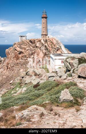 Scenario pittoresco con la vecchia torre faro e le case situate sopra Ruvida scogliera rocciosa vicino al mare sulla penisola di Capo Vilan Costa spagnola contro il cielo blu nuvoloso nella giornata estiva Foto Stock