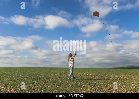 ragazza carina che corre con aquiloni in campo verde in sole giorno autunnale Foto Stock