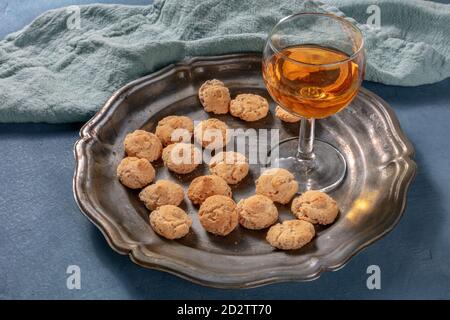 Amaretti, biscotti tradizionali italiani alle mandorle, con un bicchiere di liquore amaretto, su fondo blu scuro Foto Stock