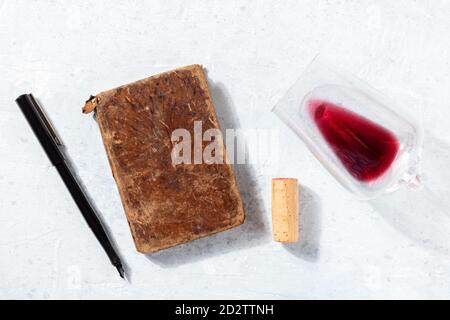 Vista dall'alto del concetto di degustazione di vini. Un vecchio taccuino, una penna, un bicchiere di vino rosso e un tappo, girato dall'alto su uno sfondo chiaro Foto Stock