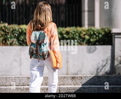 Indietro vista di anonima giovane donna con zaino e blocco note a piedi per gli studi in giornata di sole sulla strada di Madrid, Spagna Foto Stock