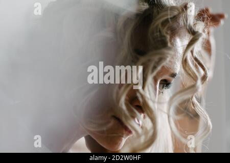 Vista laterale della donna anonima con ferro arricciacapelli a. a casa mentre si fa un elegante capelli Foto Stock