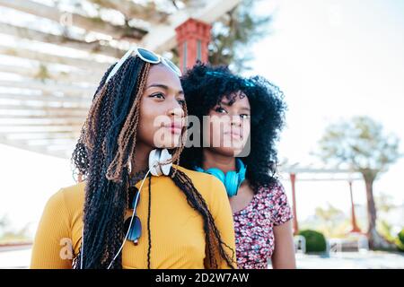 Seria donna nera con trecce in piedi vicino amico etnico femminile con capelli ricci sul lungomare in estate mentre si guarda via Foto Stock