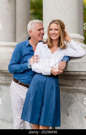 Uomo felice in piedi vicino al confine di pietra e teneramente abbracciando la donna che si appoggia sulla recinzione durante la passeggiata nel parco Foto Stock