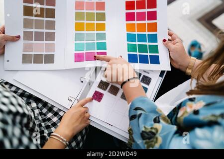 Vista dall'alto di designer femminili irriconoscibili in piedi al tavolo studio luminoso e scelta del colore dei campioni tessili Foto Stock