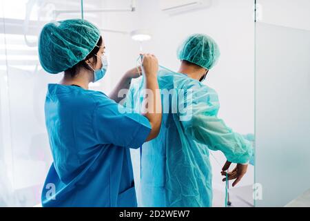 Vista posteriore dei medici di veterinario che mettono su uniforme protettiva e. guanti mentre in piedi in luminoso teatro operativo di ospedale veterinario e preparandosi per l'intervento chirurgico Foto Stock