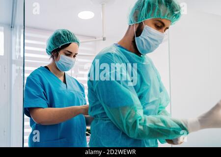 Vista laterale dei medici di veterinario che mettono su uniforme protettiva e. guanti mentre in piedi in luminoso teatro operativo di ospedale veterinario e preparandosi per l'intervento chirurgico Foto Stock