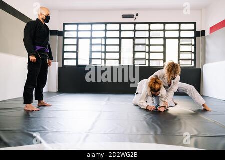 Tre partner in una formazione di arti marziali come il judo o karate con kimono. Due donne stanno praticando le tecniche sul tappetino della palestra, tutte indossando il viso ma Foto Stock