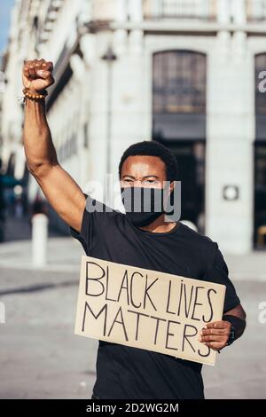 uomo che protesta a un raduno per la parità razziale in possesso di un manifesto contro il razzismo. Le vite nere contano. Foto Stock