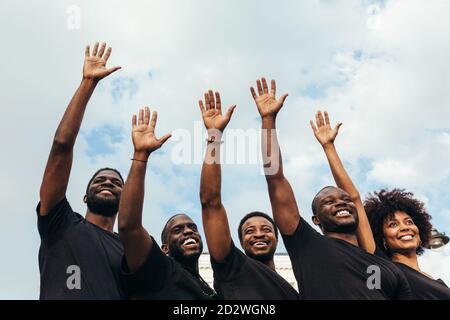 Allegri uomini neri e Donna alzando le mani contro un cielo blu Foto Stock