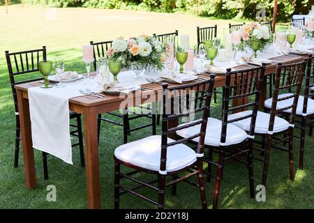 sedie e tavoli da pranzo con stoffa bianca, serviti con porcellana e bicchieri verdi. Georwedding tavolo decorato con fiori su un prato verde Foto Stock