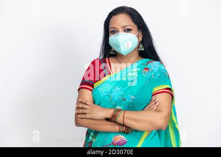 Ritratto di una donna indiana in abito tradizionale indiano, con maschera di protezione Covid 19 e in piedi contro la parete bianca, ritratto in studio, Foto Stock