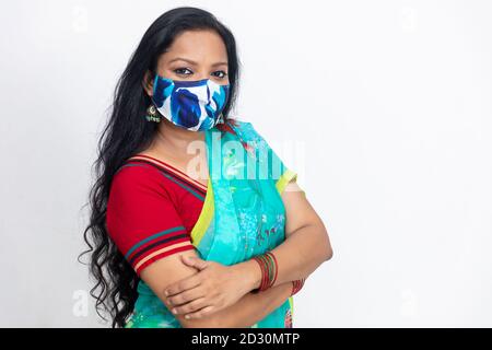 Ritratto di una donna indiana in abito tradizionale indiano, con maschera di protezione Covid 19 e in piedi contro la parete bianca, ritratto in studio, Foto Stock