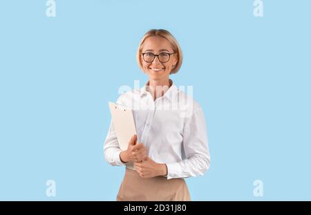 Ritratto di donna d'affari felice in abbigliamento formale e occhiali tenuta appunti su sfondo blu dello studio Foto Stock
