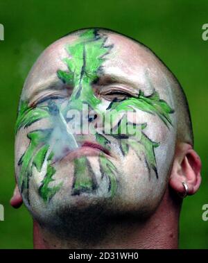 Un Cannabis Freedom Festival-goer con marijuana foglia faccia-vernice, tirando su un giunto, a Brockwell Park, Brixton, Londra, una zona in cui la polizia deve introdurre un controverso schema di dare solo un avvertimento formale alle persone trovate con una piccola quantità di droga. *...la nuova politica radicale inizia il 2 luglio e consentirà alla polizia di destinare le proprie risorse alla lotta contro le droghe più dure come la cocaina crack. 5/12/03: Un Cannabis Freedom Festival-goer con la vernice a foglia di marijuana, tirando su un giunto, a Brockwell Park, Brixton, Londra. Fumare cannabis anche per un breve periodo di tempo danneggia il Foto Stock
