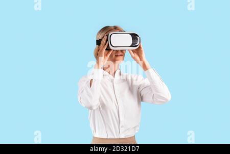 Uomo d'affari che indossa un visore VR ed esplora la realtà aumentata su blu sfondo studio Foto Stock