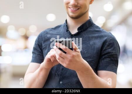 Uomo che usa lo smartphone mobile, primo piano. Immagine di un giovane uomo che usa uno smartphone mobile e sorridente. Foto Stock