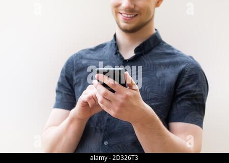 Uomo che usa lo smartphone mobile, primo piano. Immagine di un giovane uomo che usa uno smartphone mobile e sorridente. Foto Stock