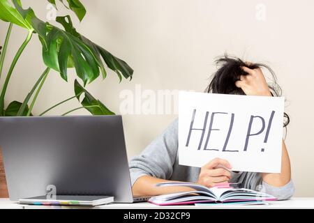 Stanco frustrato donna seduta al tavolo e tenendo la carta con aiuto di parola. Lavorare online, imparare da casa Foto Stock