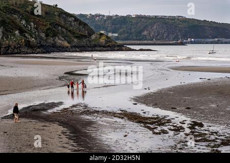 Una famiglia attraversa la spiaggia a bassa marea nel porto di Lower Fishguard, Pembrokeshire, Galles, Regno Unito Foto Stock