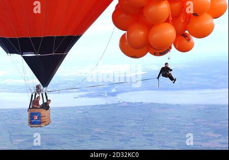 Mike Howard che penzolante sotto centinaia di palloncini pieni di elio alla Bristol Balloon Fiesta. Howard, vestito da suo eroe temerario in una giacca da cena, è salito a più di 7.000 piedi ma non è riuscito a salire abbastanza in alto per rompere il record mondiale di 11.000 piedi a causa della copertura pesante della nuvola. Foto Stock